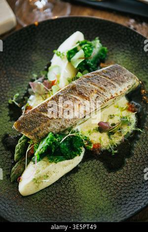Ein kunstvoll überzogenes Fischgericht, garniert mit frischem Gemüse und Sauce, bietet ein köstliches Erlebnis Stockfoto