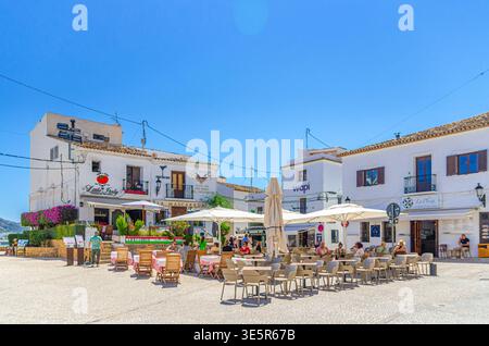 Altea, Spanien, 30. Mai 2025: Die Menschen entspannen sich im Straßenrestaurant im Außencafé auf dem Platz der Kirche Plaza de la Iglesia mit typischem weißem Haus in o Stockfoto