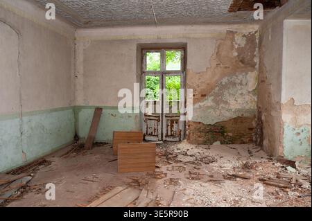 Verlassener Raum Mit Abblätternder Farbe, Kaputten Fenstern, Schutt Und Boden, Freiliegende Ziegelwände, Bewachsenes Grün Draußen, Vintage Decay Style Stockfoto