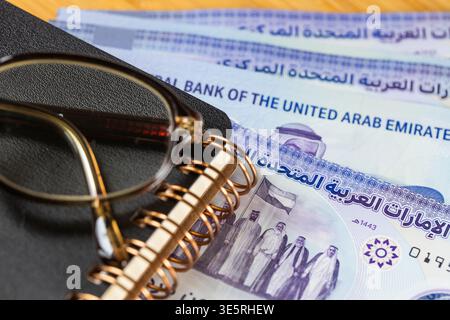 Geld der Vereinigten Arabischen Emirate. Bewertung des Finanzmarktes in Dubai. Dirhams, Brillen und ein Business-Notizbuch. Finanzkonzept. Nahaufnahme Stockfoto