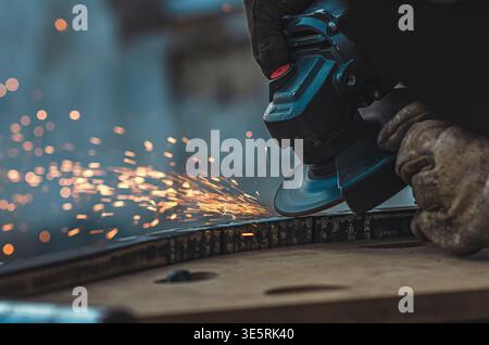 Nahaufnahme des Werkers mit Winkelschleifer zum Glätten der Metalloberfläche. Helle Funken fliegen, während die rotierende Scheibe die Kante verfeinert und Präzision, Kontrolle und unterstreicht Stockfoto