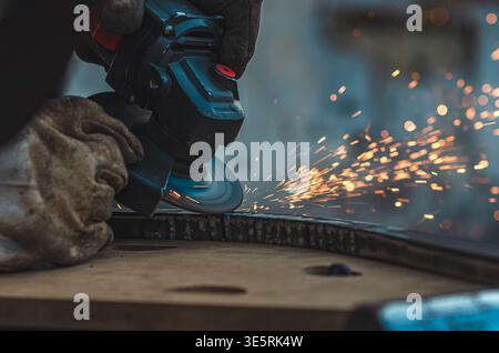 Nahaufnahme des Werkers mit Winkelschleifer zum Glätten der Metalloberfläche. Helle Funken fliegen, während die rotierende Scheibe die Kante verfeinert und Präzision, Kontrolle und unterstreicht Stockfoto