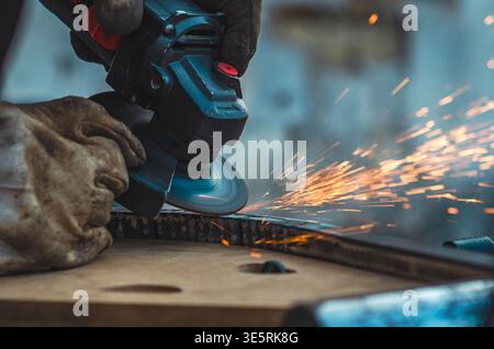 Nahaufnahme des Werkers mit Winkelschleifer zum Glätten der Metalloberfläche. Helle Funken fliegen, während die rotierende Scheibe die Kante verfeinert und Präzision, Kontrolle und unterstreicht Stockfoto