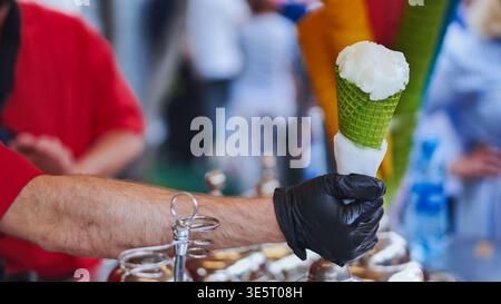 Hand des Verkäufers in schwarzem Handschuh präsentiert eine grüne Waffelkegel mit weißem Eis Stockfoto