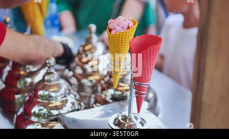 Erdbeer-Eiskugeln in gelben und roten Waffelkegeln an einem Eisstand unter freiem Himmel Stockfoto