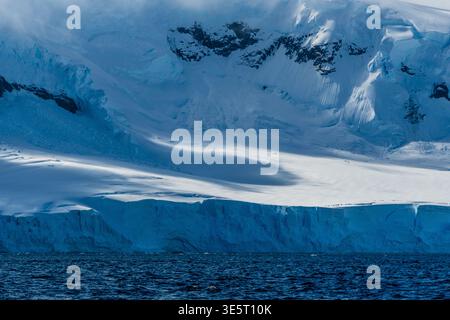 Eine beschauliche antarktische Landschaft in der Nähe des Hafens Mikkelsen auf Trinity Island, mit starken Reflexen, zerklüfteten Bergen und beeindruckenden Eisbergen Stockfoto