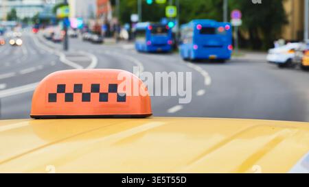 Gelbes Taxischild auf dem Dach mit städtischem Straßenverkehr und verschwommenen Bussen Stockfoto