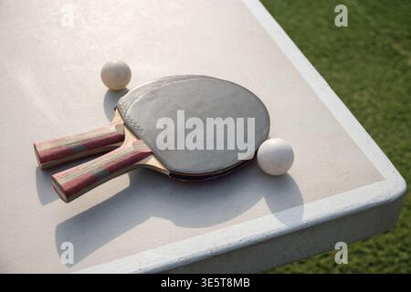 Tischtennisschläger und -Bälle auf einem Tisch im Freien bei Sonnenlicht für sportliche Aktivitäten, Freizeit- und Hobbykonzepte Stockfoto
