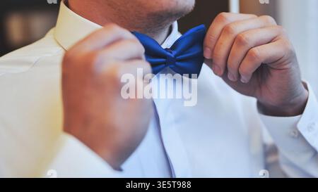 Nahaufnahme eines Bräutigams in einem weißen Hemd, der seine blaue Fliege anpasst. Vorbereitung des Hochzeitstages auf eine formelle Zeremonie. Stockfoto