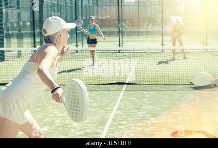 Entschlossene, sportliche, ältere Frau, die ihr Bestes gibt, wenn sie vor Gericht Padel spielt Stockfoto
