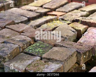 Nahaufnahme von verwitterten Altsteinen mit Moos- und Mörtelrückständen. Blick von oben auf farbenfrohe gesammelte Tonziegel für rustikale Bauten oder Kap Stockfoto
