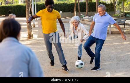 Fröhliche Gruppe von Menschen mittleren und älteren Alters mit gemischtem Rennen, die im Freien Fußballspiele spielen Stockfoto