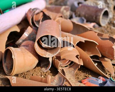 Gebrochene keramische Abflussrohre auf der Baustelle, Haufen zersplitterter Tonklärrohre, Industriestruß, orangene Terrakotta-Rohrfragmente Stockfoto