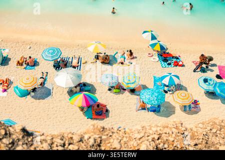 Blick aus der Vogelperspektive auf den überfüllten Sandstrand mit farbenfrohen Sonnenschirmen und Sonnenanbetern, die Sommerurlaub an der türkisfarbenen Küste genießen Stockfoto