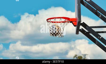 Basketball, der durch den Korb schwingt, mit Wolken im Hintergrund Stockfoto