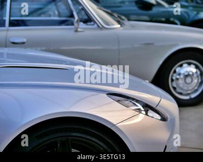 Nahaufnahme von Luxussportwagen, die hintereinander geparkt sind. Der Schwerpunkt liegt auf der eleganten silbernen Motorhaube und dem modernen LED-Scheinwerfer eines modernen Supersportwagens im Vorderteil Stockfoto