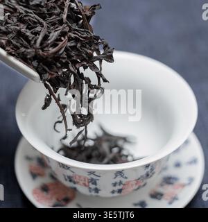 Wunderschöne dunkle schwarze Teeblätter werden sorgfältig in eine feine, elegante chinesische Teetasse gegossen Stockfoto