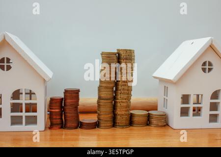 Ein konzeptionelles Bild mit zwei Miniaturmodellhäusern, eingebettet zwischen großen Stapeln und Häufern von Kupfer-Euro-Cent-Münzen, symbolisiert Immobilieninvestitionen Stockfoto