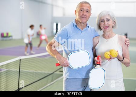 Porträt eines positiven älteren Ehepaares nach dem Spielen von Pickleball mit Schlägern in der Hand Stockfoto