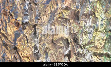 Oberfläche aus zerknitterter Aluminiumfolie, die Metallic-Farben und abstrakte Lichtstrukturen reflektiert Stockfoto