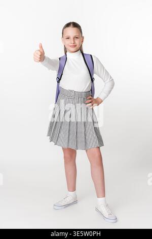 Porträt eines glücklichen Jugendlichen Schülers in stylischer Uniform mit Rucksack, mit Daumen nach oben. Sauberer weißer Hintergrund. Positive Stimmung und b Stockfoto
