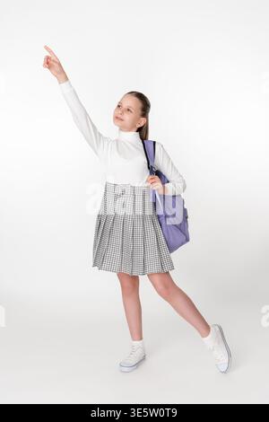 Langporträt eines hoffnungsvollen Jugendschülers in Schuluniform mit lila Rucksack. Das Schulmädchen zeigt nach oben und blickt in die Zukunft. Isolierter o Stockfoto