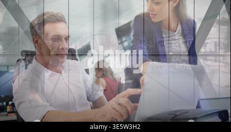 Seniorin in leichtem Hemd bedient Touchscreen im Büro, Frau im Blazer beugt sich und zeigt Stockfoto