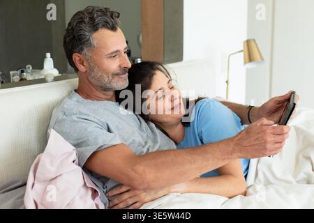 Ein Paar, das sich auf dem Bett liegend, ein Mann in der Hand, eine Frau, die sich auf die Brust lehnt, umgeben von Kissen Stockfoto