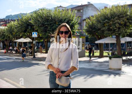 Junge Frau mit Sonnenbrille, die auf der sonnigen Straße in Asturien steht Stockfoto