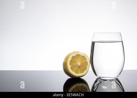 Geschnittene Zitrone neben Glas klarem Wasser auf weißem Hintergrund mit Kopierraum Stockfoto