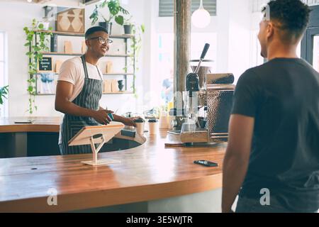 Gast, glücklich und Leute im Coffee Shop an der Theke für Service mit Getränk, Getränk und Bestellung. Restaurant, Cafeteria und Mann, der mit dem Barista spricht Stockfoto