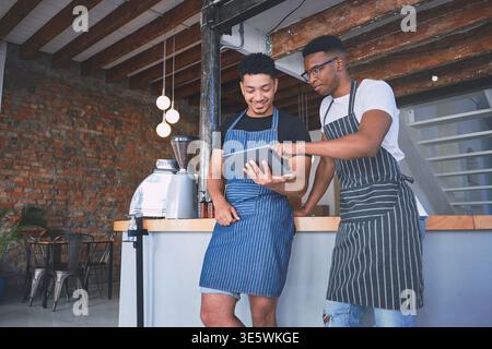 Kellner, Männer und unterhalten sich mit dem Tablet im Café für die Bewertungen der Webseite, Online-Verkäufe und Menüaktualisierungen. Kleine Unternehmen, Barista und Team mit Technik für Stockfoto