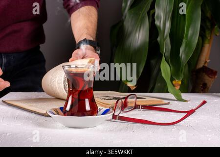 Mann rührt türkischen Tee in traditionellem Glasbecher zu Hause Stockfoto