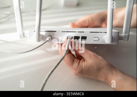 Nahaufnahme einer Person, die ein ethernet-rj45-Kabel und ein Netzteil an einen Wireless-Router mit Antennen angeschlossen hat. Konzept der Internet-Installation, Tech Stockfoto