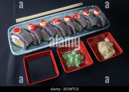 Gourmet-Sushi-Rolls mit schwarzem Reis, frischen Garnelen, cremiger Sauce und roter Kaviar-Garnele serviert auf einer eleganten Keramikplatte - ideal für Luxus Stockfoto
