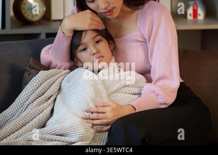 Mutter tröstet ihr krankes Kind auf einer Couch Stockfoto