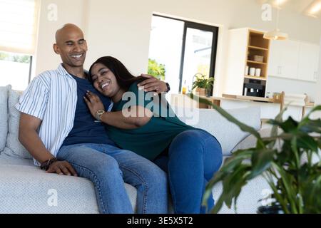 Afroamerikanisches Paar sitzt auf einem hellen Sofa im modernen Wohnzimmer und kuschelt an der Zimmerpflanze Stockfoto
