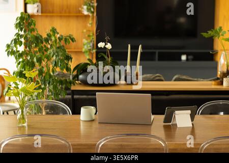Heim-Arbeitsplatz mit langem hölzernem Esstisch mit Laptop-Mitte, Tablet und Becher in der Nähe Stockfoto
