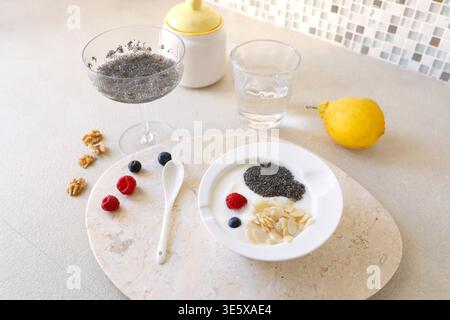 Gesundes Frühstück mit Joghurt Chia Samen und frischen Beeren in weißer Schüssel auf Marmortablett. Der Hochwinkelschuss umfasst Chia Pudding Zitrone und Walnüsse Stockfoto