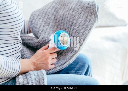 Abgeschnittene Frau, die Pillen aus grauem Strickgewebe mit einem Elektrorasierer entfernt Stockfoto
