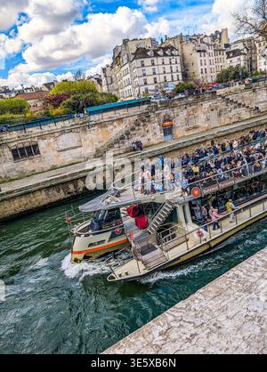 Ein überfülltes Sightseeing-Boot gleitet entlang der seine unter historischen Brücken und bietet Touristen eine malerische Wasserstraßentour durch Paris, Frankreich Stockfoto