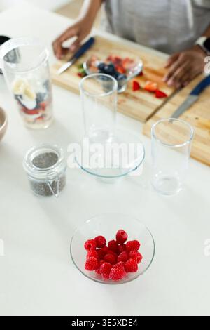 Afroamerikanerin, die Obst auf der Küchenzeile mit Glasschale Himbeeren und Messer zubereitete Stockfoto