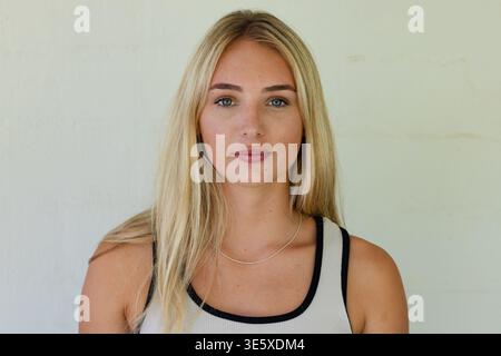 Eine Erwachsene Frau posiert und schaut in die Kamera im Studio, trägt ein geripptes Tanktop und eine silberne Kette Stockfoto