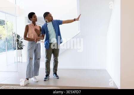 Ein vielseitiges Paar, das eine leere Wand in einem modernen Haus mit Topfpflanzen und Glastür untersucht Stockfoto