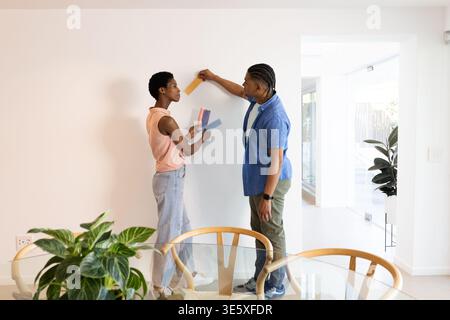 Wir vergleichen verschiedene Paare, die Farbmuster an der weißen Wand im Essbereich mit Glastisch auswählen Stockfoto
