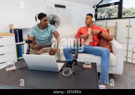 Aufnahme verschiedener männlicher Freunde, die Podcasts auf Sofa im Home Office diskutieren, mit Laptop und Mikrofonen Stockfoto
