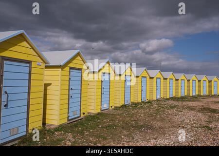 Reihe von gelben Strandhütten mit blauen Türen entlang der Küste im Küstenort Littlhampton West Sussex England Großbritannien Stockfoto