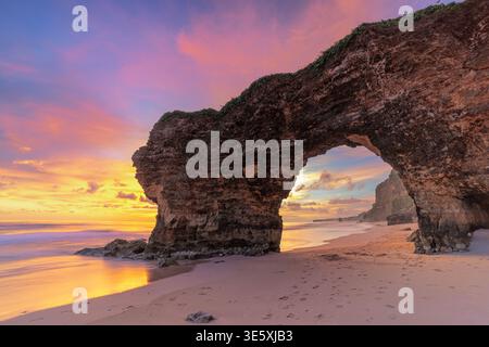 Dramatischer Sonnenuntergang durch den berühmten Natursteinbogen am Mbawana Beach im Südwesten von Sumba, Indonesien, unter einem lebendigen, farbenfrohen Himmel Stockfoto