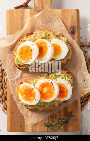 Zwei Scheiben geröstetes Sauerteigbrot mit Avocadopüree und marmeliert weich gekochten Eierscheiben. Aufnahmen aus einem großen Winkel mit natürlichem, hellem Licht Stockfoto