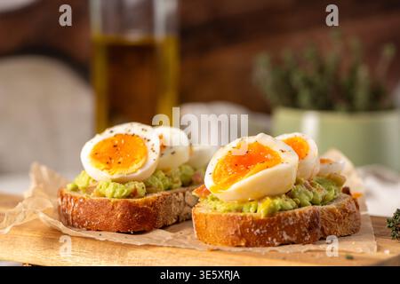 Zwei Scheiben knuspriger Sauerteig, belegt mit zerstoßener Avocado und marmelierten weichen gekochten Eiern. Warme, natürliche Beleuchtung unterstreicht die cremige Textur und die rustikale Atmosphäre Stockfoto
